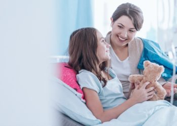 Sisters smiling and lying in bed in the hospital together. Family support during illness concept