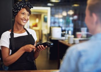Smiling attractive African American small business owner taking payment from a customer processing a credit card through the handheld banking machine