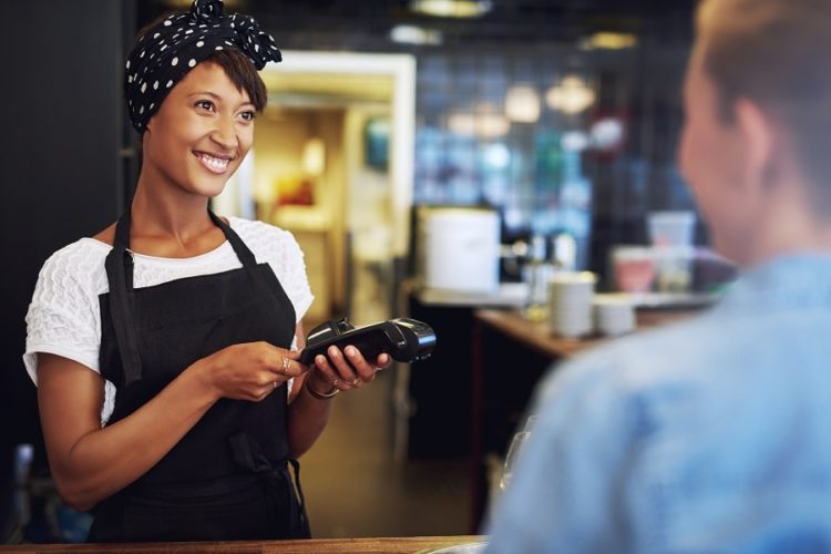 Smiling attractive African American small business owner taking payment from a customer processing a credit card through the handheld banking machine