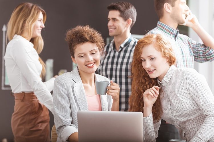 Women working together on laptop, business team in background