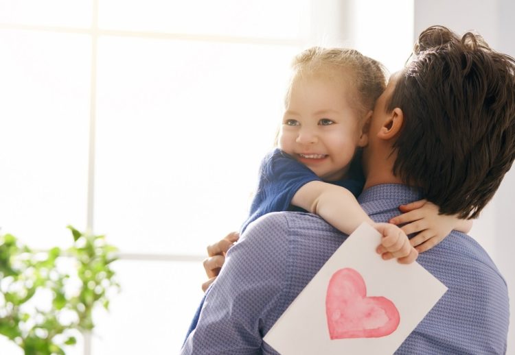Happy father's day! Child daughter congratulating dad and giving him postcard. Daddy and girl smiling and hugging. Family holiday and togetherness.