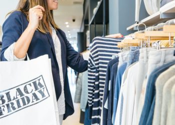 Side view of a woman looking through clothing rack and holding Black Friday bag